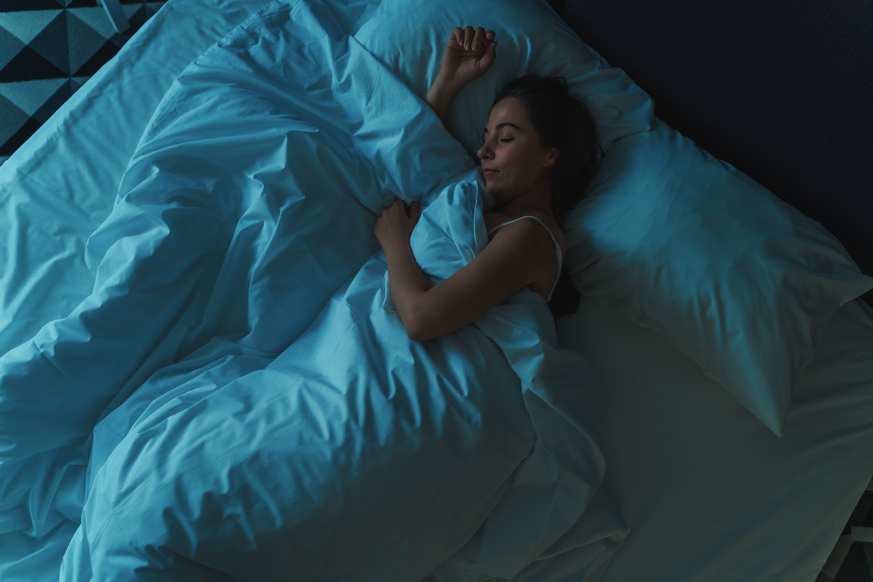 Woman sleeping in a dark room with blue lighting on a bed.