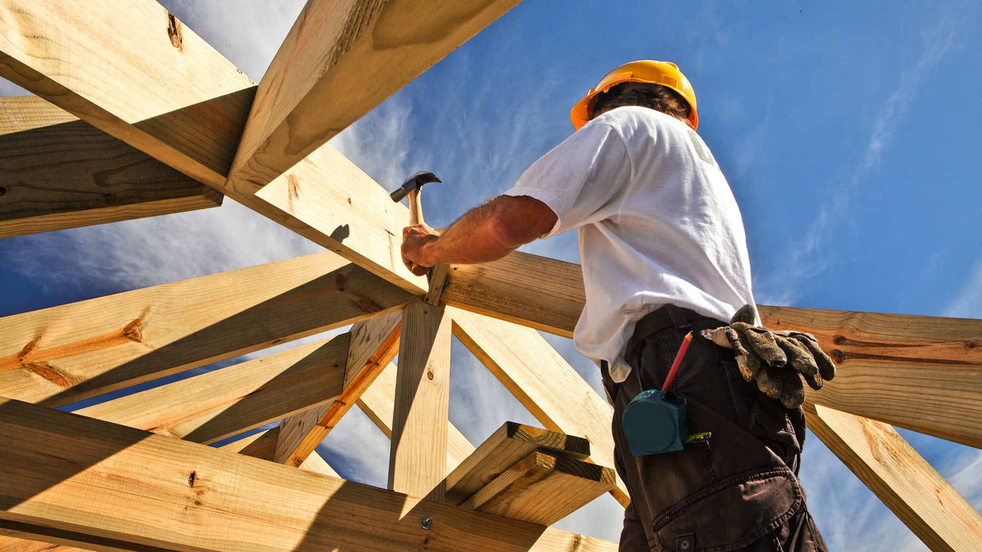 Worker assembling wooden beams against a blue sky