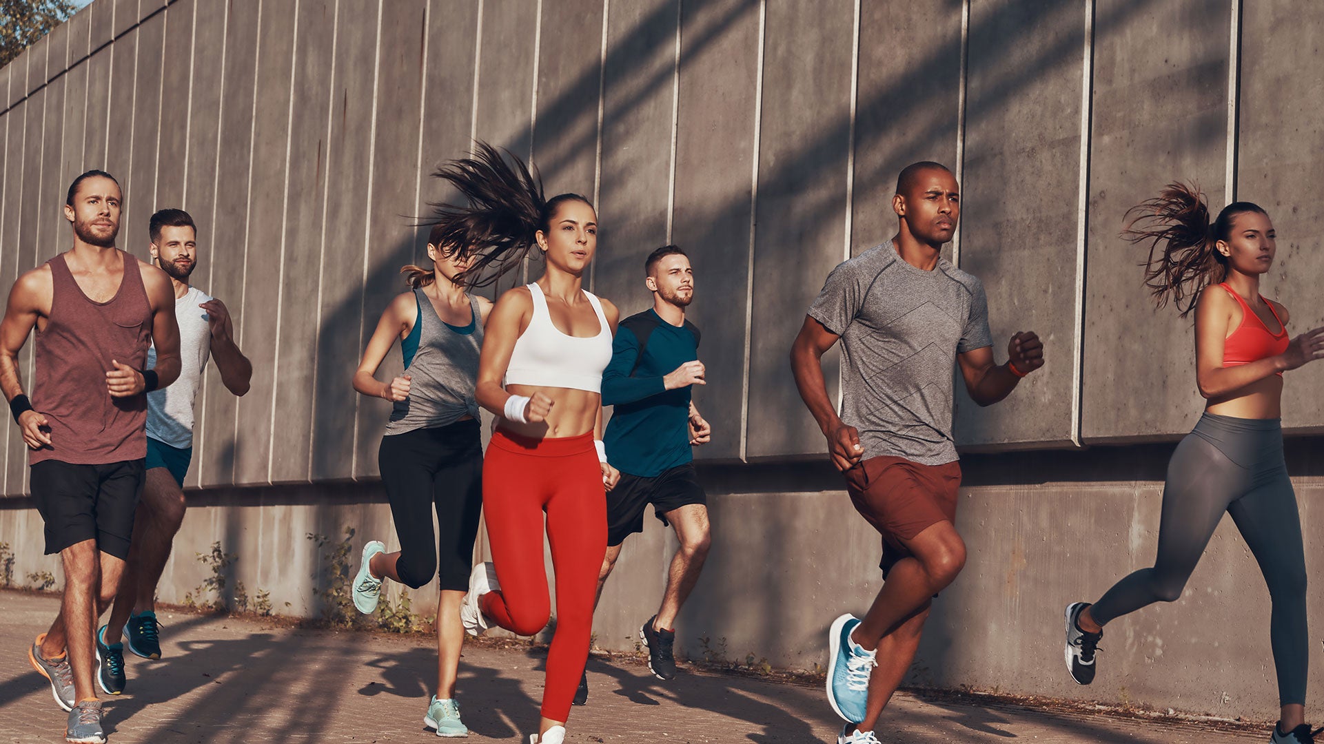 Group of runners in athletic wear running outdoors against a concrete wall.