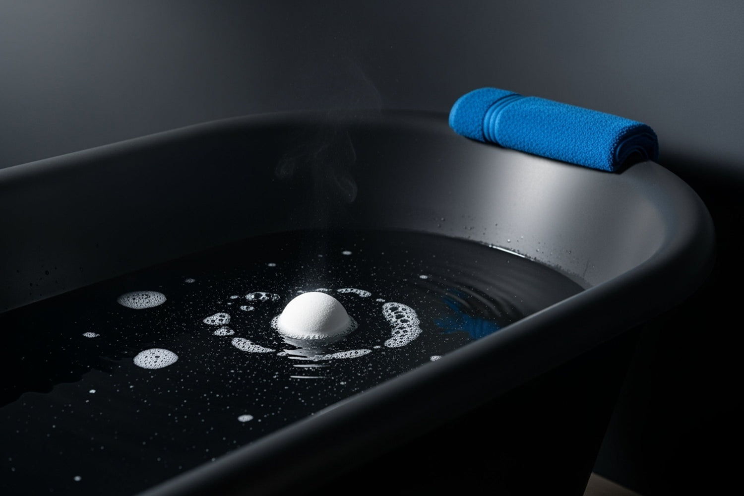 White bath bomb fizzing in a dark bathtub with steam and blue towel on the edge.