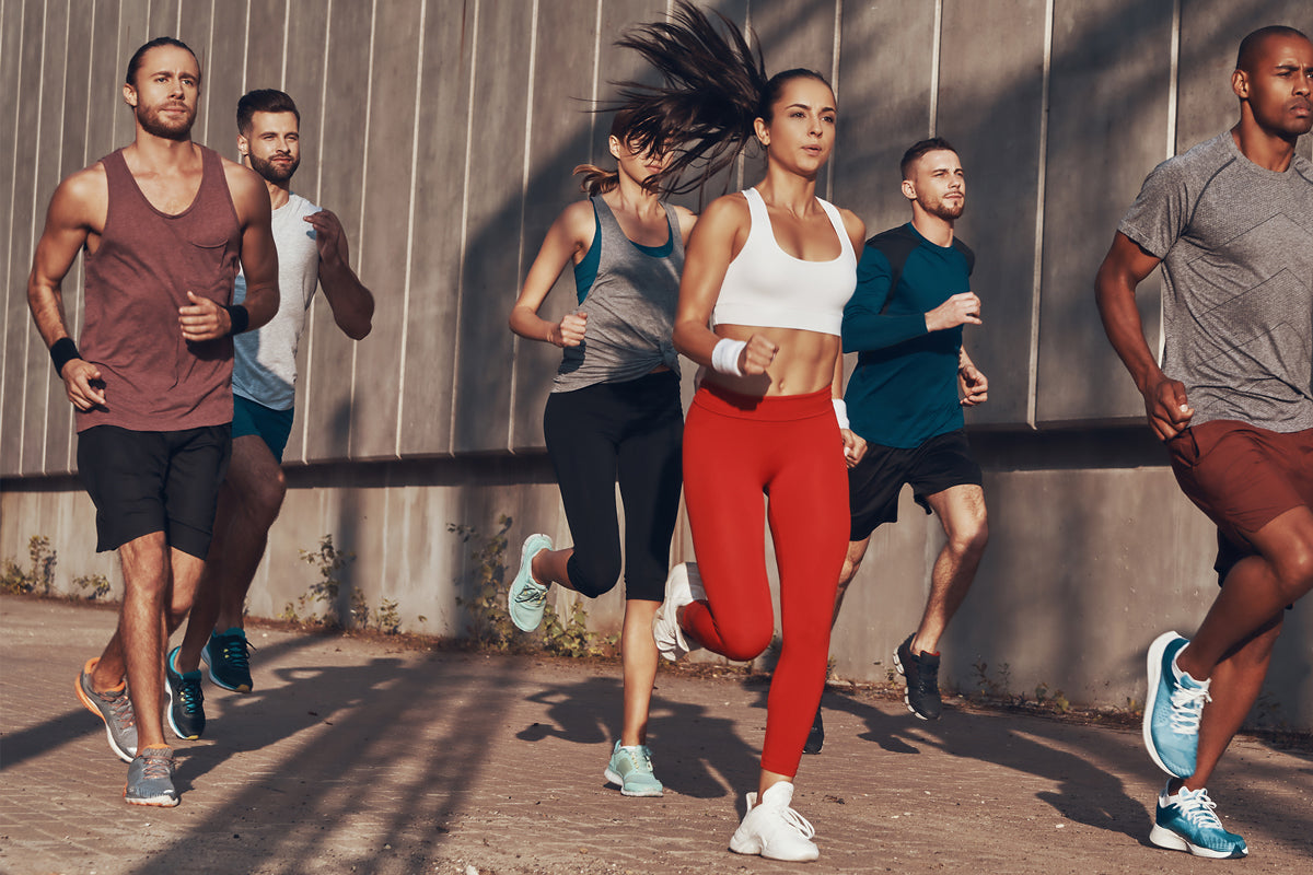 A diverse group of athletes running outdoors in activewear, focused on fitness and endurance training. They stride together in sunlight, representing energy, teamwork, and recovery after intense workouts.